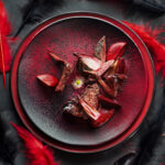 Plato de pollo artístico con fondo de plumas rojas, estilo conceptual.