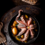 Pulpo servido en cazuela con papas y un ojo simbólico en el centro.